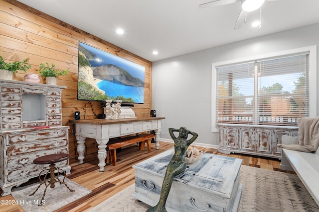 living area featuring ceiling fan, wooden walls, and light hardwood / wood-style flooring