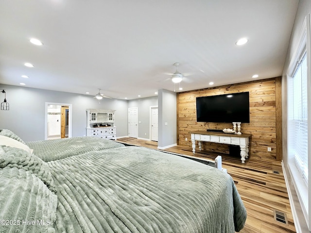 bedroom featuring ceiling fan, wooden walls, and light hardwood / wood-style flooring