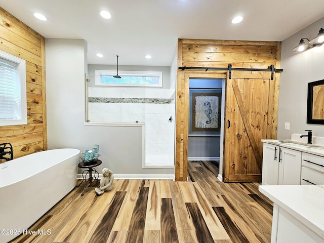 bathroom featuring hardwood / wood-style flooring, vanity, wood walls, and plus walk in shower