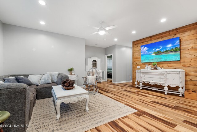 living room featuring ceiling fan, wooden walls, and light wood-type flooring