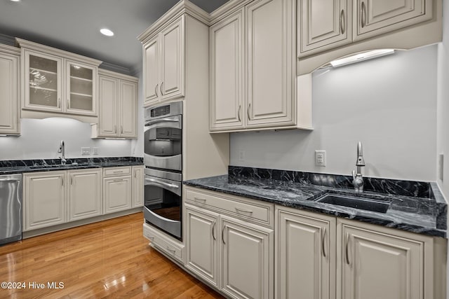 kitchen featuring light wood-type flooring, sink, dark stone counters, and stainless steel appliances