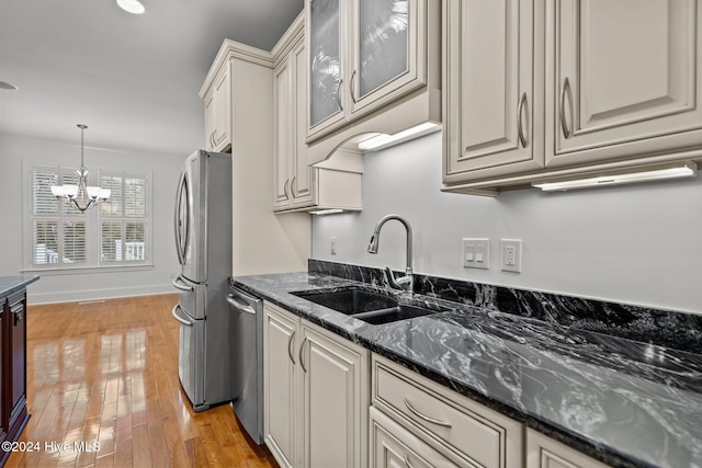 kitchen featuring sink, dark stone countertops, light hardwood / wood-style floors, stainless steel appliances, and a chandelier