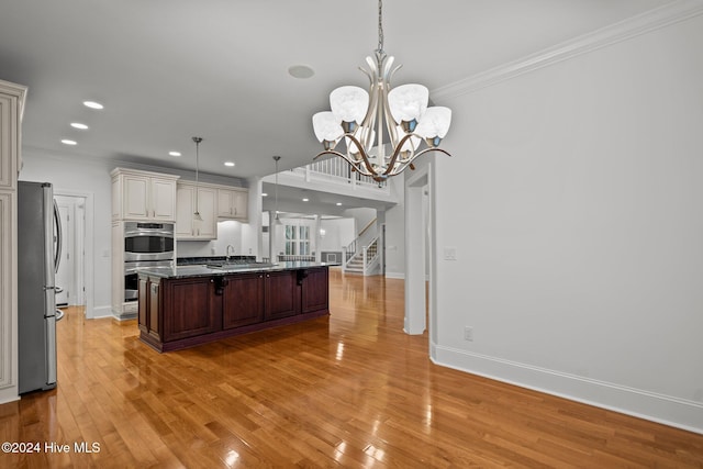 kitchen featuring a chandelier, decorative light fixtures, a center island with sink, appliances with stainless steel finishes, and light wood-type flooring