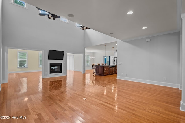 unfurnished living room with crown molding, light hardwood / wood-style flooring, a high ceiling, and a notable chandelier