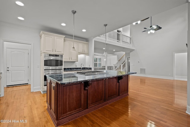 kitchen featuring ceiling fan, dark stone counters, pendant lighting, appliances with stainless steel finishes, and light wood-type flooring