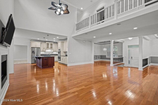 unfurnished living room with crown molding, light hardwood / wood-style flooring, ceiling fan with notable chandelier, and a high ceiling