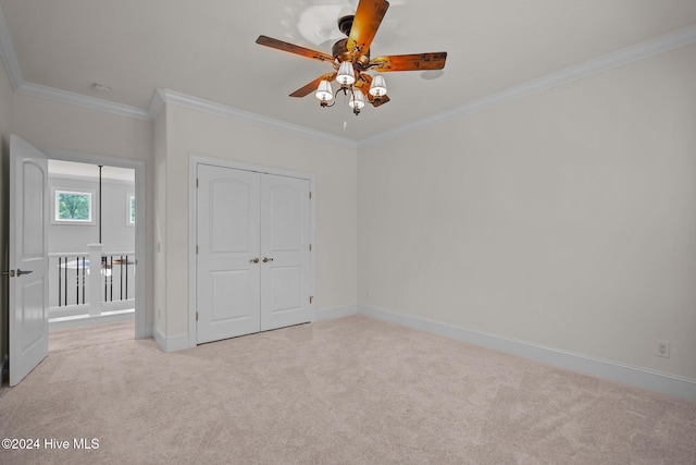 unfurnished bedroom with crown molding, a closet, ceiling fan, and light colored carpet