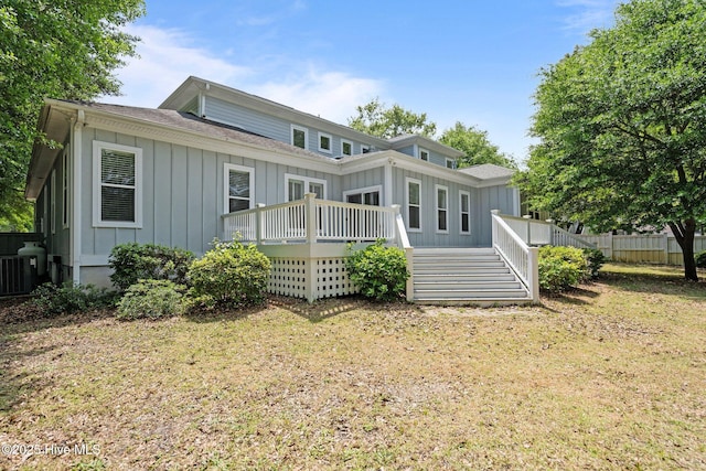 rear view of house featuring board and batten siding, roof with shingles, a lawn, a deck, and fence