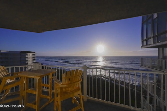 balcony at dusk featuring a view of the beach and a water view