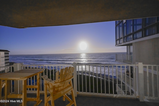 balcony at dusk featuring a water view and a beach view