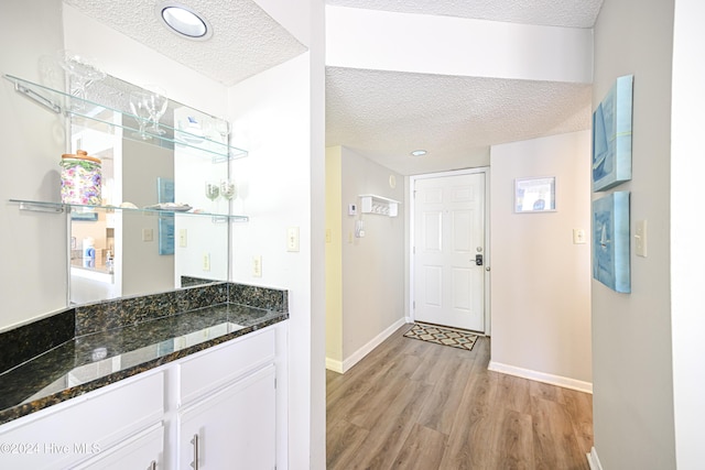 interior space featuring white cabinets, dark stone countertops, a textured ceiling, and light hardwood / wood-style flooring