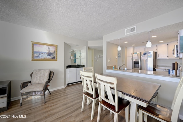 dining area with a textured ceiling, light hardwood / wood-style flooring, and sink