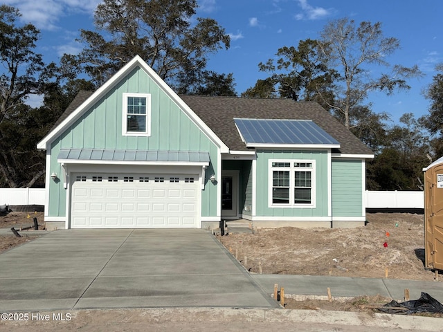 view of front of house with a garage, driveway, a shingled roof, solar panels, and board and batten siding