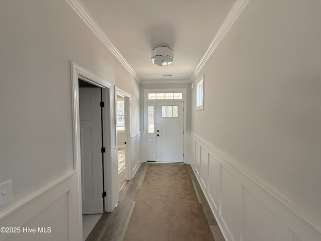 doorway with ornamental molding, a healthy amount of sunlight, wainscoting, and a decorative wall