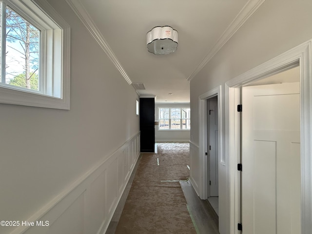 corridor featuring wainscoting, dark carpet, a decorative wall, and ornamental molding