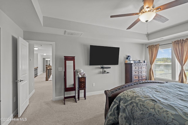 bedroom with light carpet, a tray ceiling, and ceiling fan