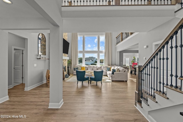 foyer featuring a stone fireplace, a towering ceiling, and light wood-type flooring