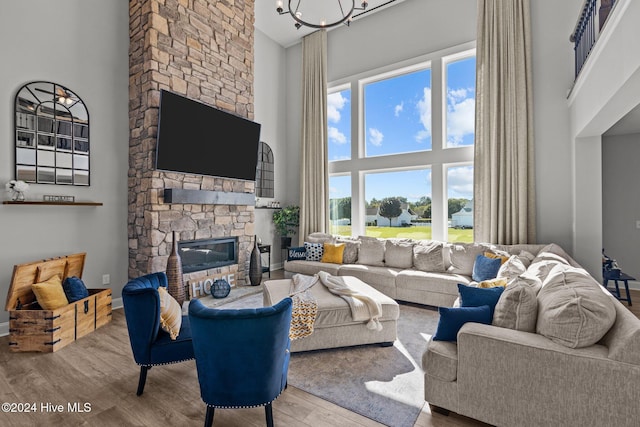 living room with a stone fireplace, hardwood / wood-style floors, a high ceiling, and an inviting chandelier