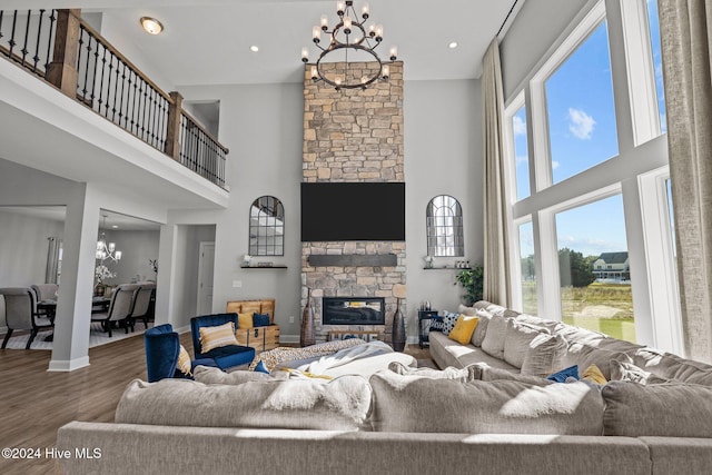 living room featuring a stone fireplace, a towering ceiling, a notable chandelier, and hardwood / wood-style flooring