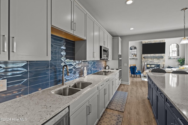 kitchen with sink, hanging light fixtures, stainless steel appliances, a stone fireplace, and wood-type flooring