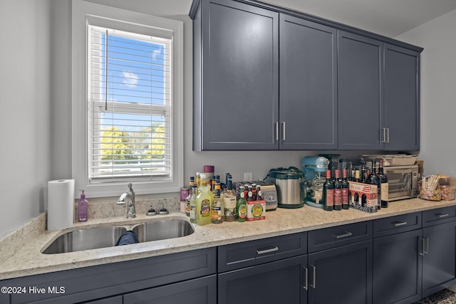 kitchen with gray cabinetry, light stone countertops, and sink