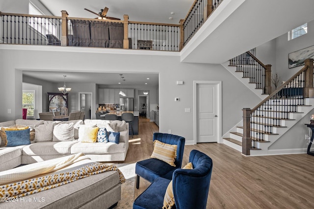 living room featuring ceiling fan with notable chandelier, a high ceiling, and hardwood / wood-style flooring