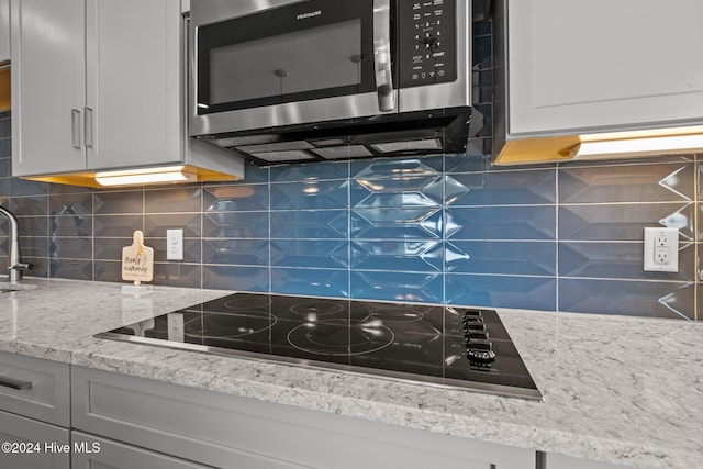 kitchen with backsplash, black electric cooktop, and light stone countertops