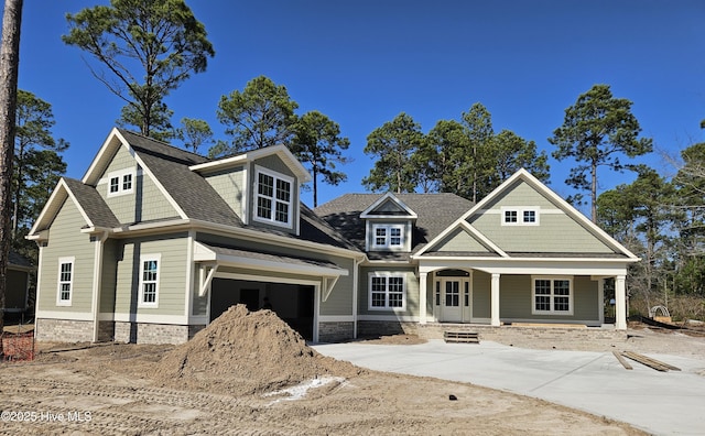 view of front of home featuring a garage, concrete driveway, a porch, and roof with shingles