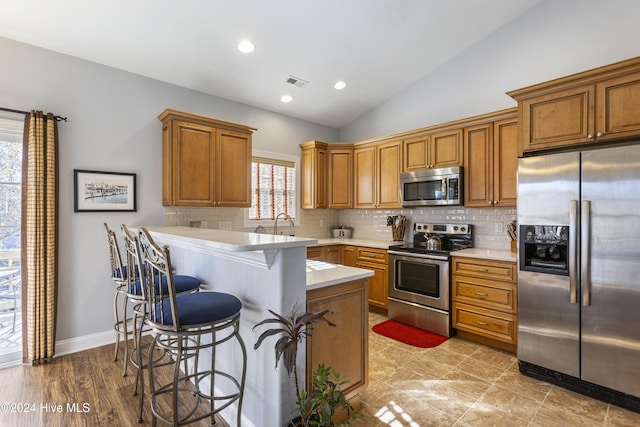 kitchen with a breakfast bar, lofted ceiling, backsplash, appliances with stainless steel finishes, and kitchen peninsula