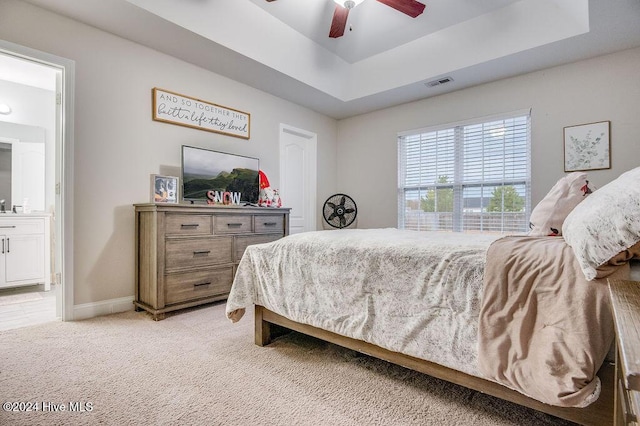 carpeted bedroom with ensuite bathroom, ceiling fan, and a raised ceiling