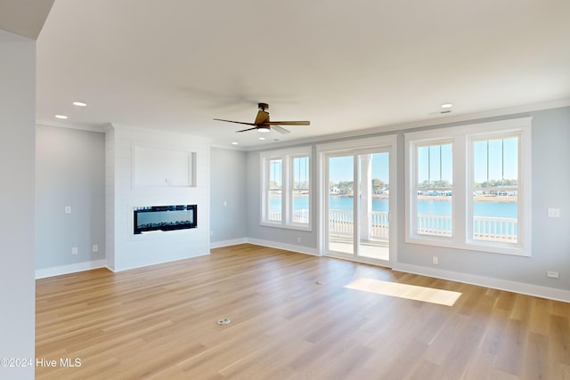 unfurnished living room featuring a water view, crown molding, ceiling fan, light wood-type flooring, and a fireplace