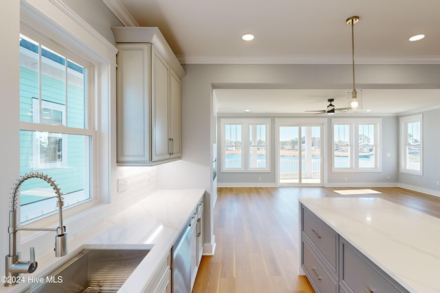 kitchen with light stone countertops, ceiling fan, sink, decorative light fixtures, and light hardwood / wood-style flooring