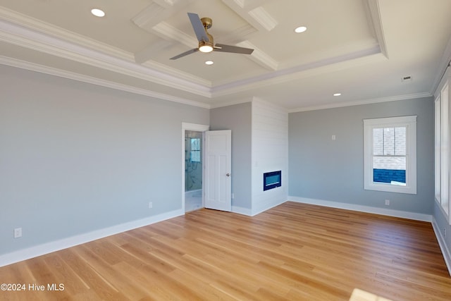 spare room featuring coffered ceiling, ceiling fan, light wood-type flooring, ornamental molding, and a large fireplace