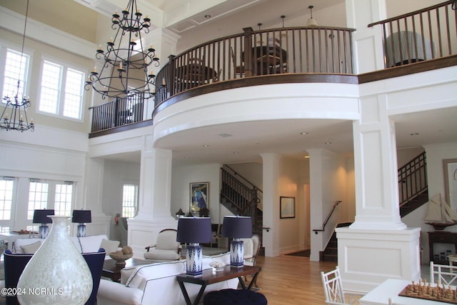 living room with decorative columns, a towering ceiling, a healthy amount of sunlight, and light wood-type flooring