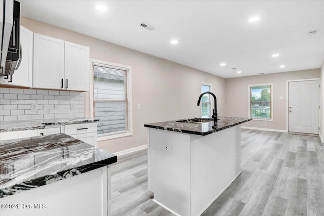 kitchen featuring tasteful backsplash, a kitchen island with sink, sink, and white cabinets