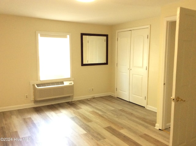 unfurnished bedroom featuring a wall mounted air conditioner, light hardwood / wood-style floors, and a closet
