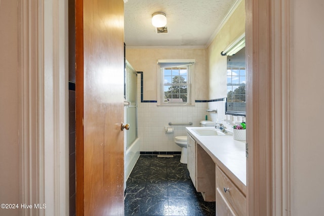 full bathroom with tile walls, bath / shower combo with glass door, vanity, a textured ceiling, and toilet