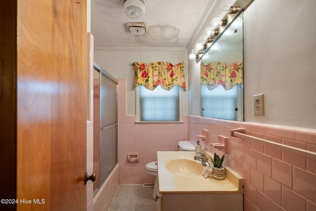 full bathroom with ornamental molding, combined bath / shower with glass door, tile walls, and vanity