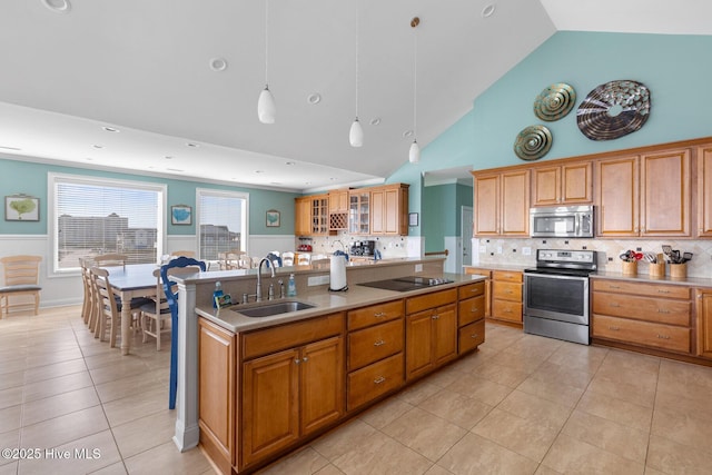 kitchen with appliances with stainless steel finishes, decorative light fixtures, light tile patterned floors, sink, and a kitchen island with sink