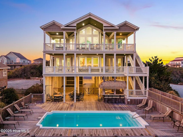 back house at dusk featuring a pool side deck, an outdoor bar, and a balcony