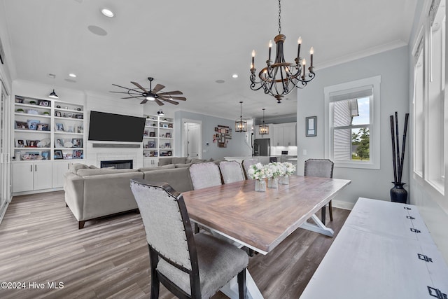 dining area with ceiling fan with notable chandelier, built in features, a fireplace, light hardwood / wood-style floors, and crown molding