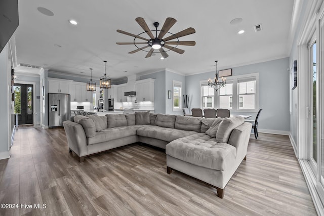 living room featuring ornamental molding, sink, ceiling fan with notable chandelier, and light wood-type flooring