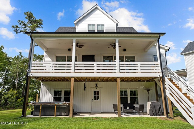 back of property with a lawn, ceiling fan, a patio, a wooden deck, and a hot tub