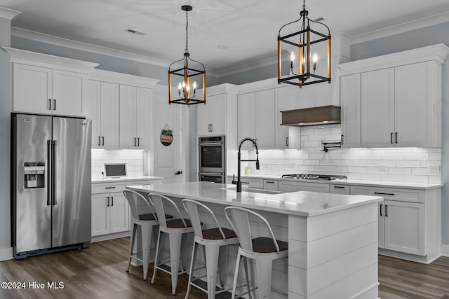 kitchen featuring appliances with stainless steel finishes, decorative light fixtures, white cabinetry, sink, and a kitchen island with sink