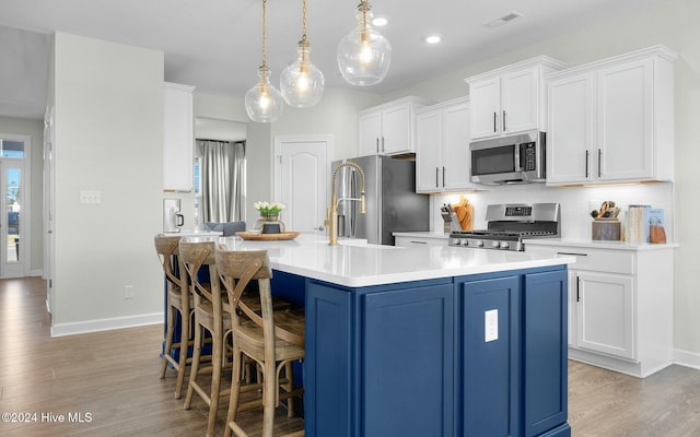 kitchen with stainless steel appliances, a kitchen island with sink, white cabinets, and decorative light fixtures