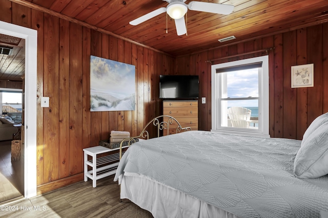 bedroom with multiple windows, ceiling fan, hardwood / wood-style floors, and wood walls