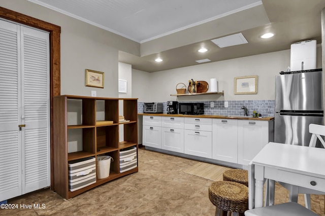 kitchen featuring stainless steel fridge, backsplash, ornamental molding, butcher block countertops, and white cabinetry