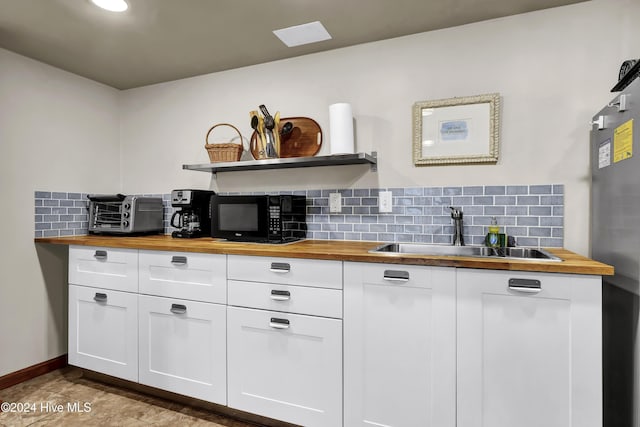 kitchen with tasteful backsplash, butcher block counters, white cabinetry, and sink