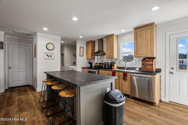 kitchen featuring appliances with stainless steel finishes, a center island, a healthy amount of sunlight, and wall chimney range hood