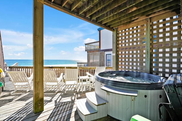 wooden deck featuring a view of the beach, a hot tub, and a water view